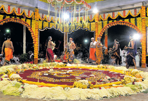 An intricate Naga Mandala drawn on the ground in red, yellow, white and green natural powders, showing interwoven serpents