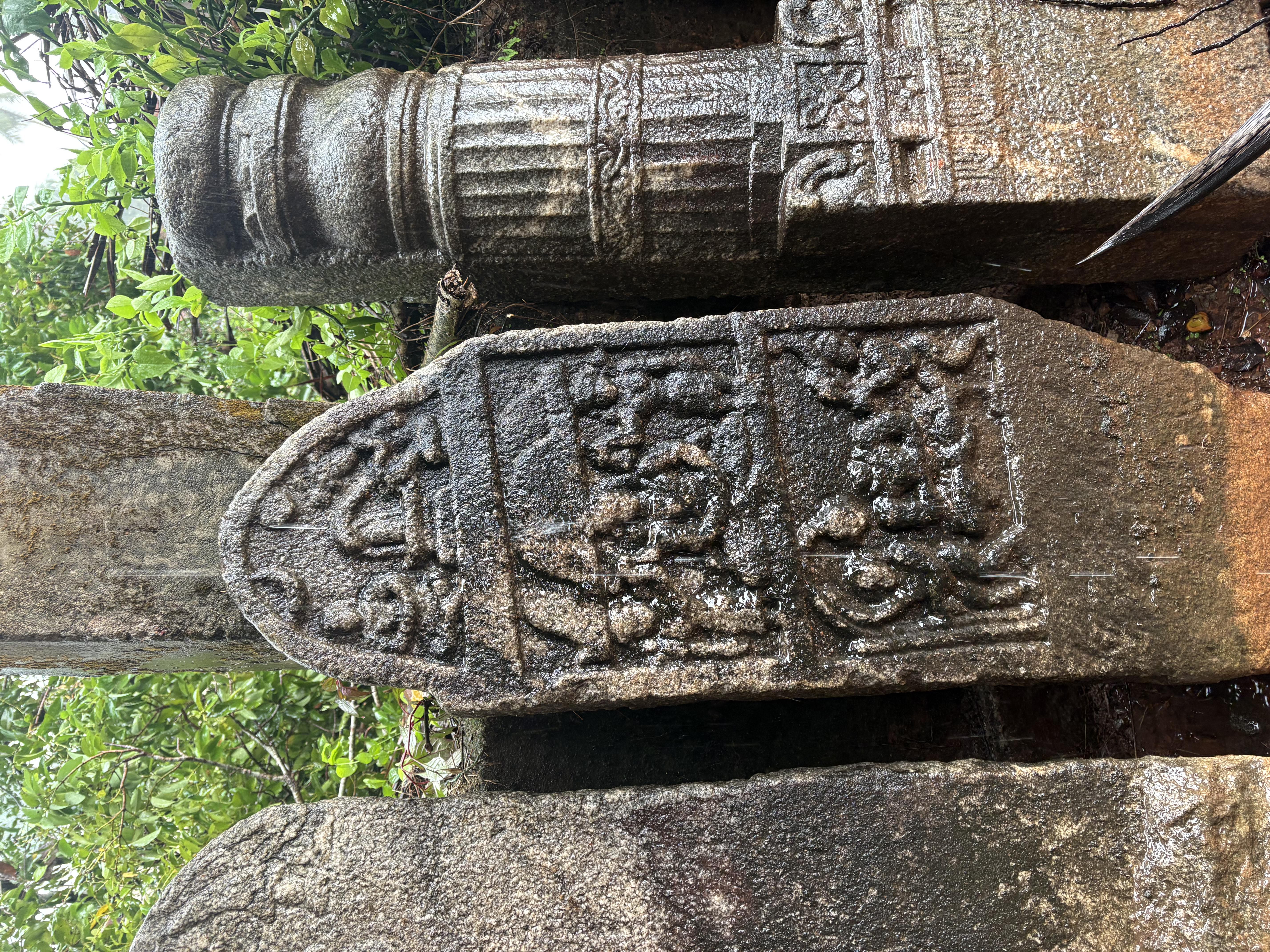 A hero-stone with figural panels beside a monolithic pillar