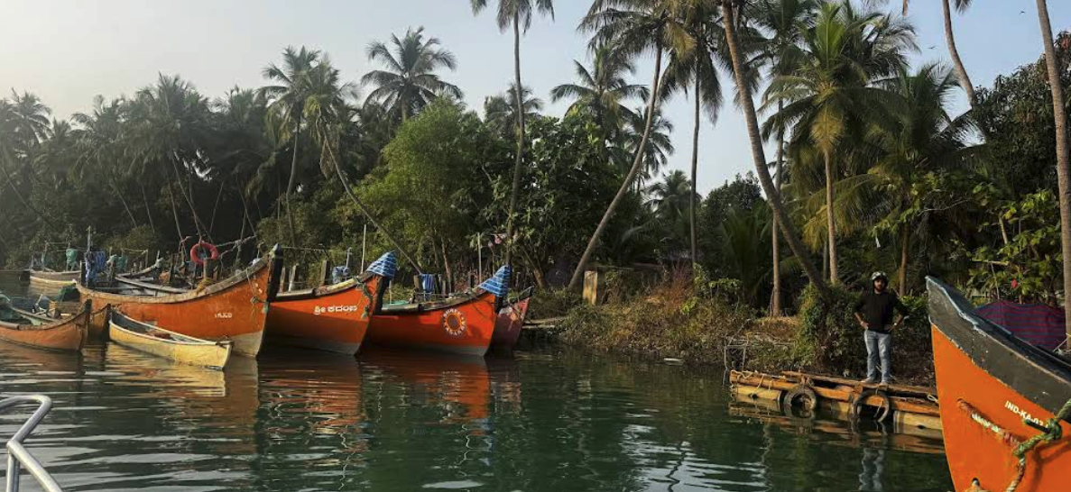 A fisherman beside orange fishing boats moored under coconut palms on the riverbank